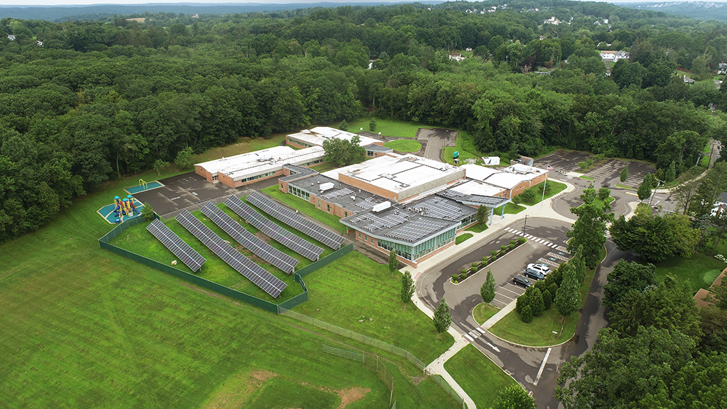Arial view of the South Windsor school with solar panels installed on the ground behind the building  